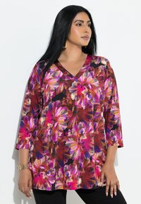 Kwiatowa tunika z dekoltem w kształcie litery V, z żywymi różowymi i fioletowymi kwiatami na czarnym tle. Długie rękawy i luźny krój.