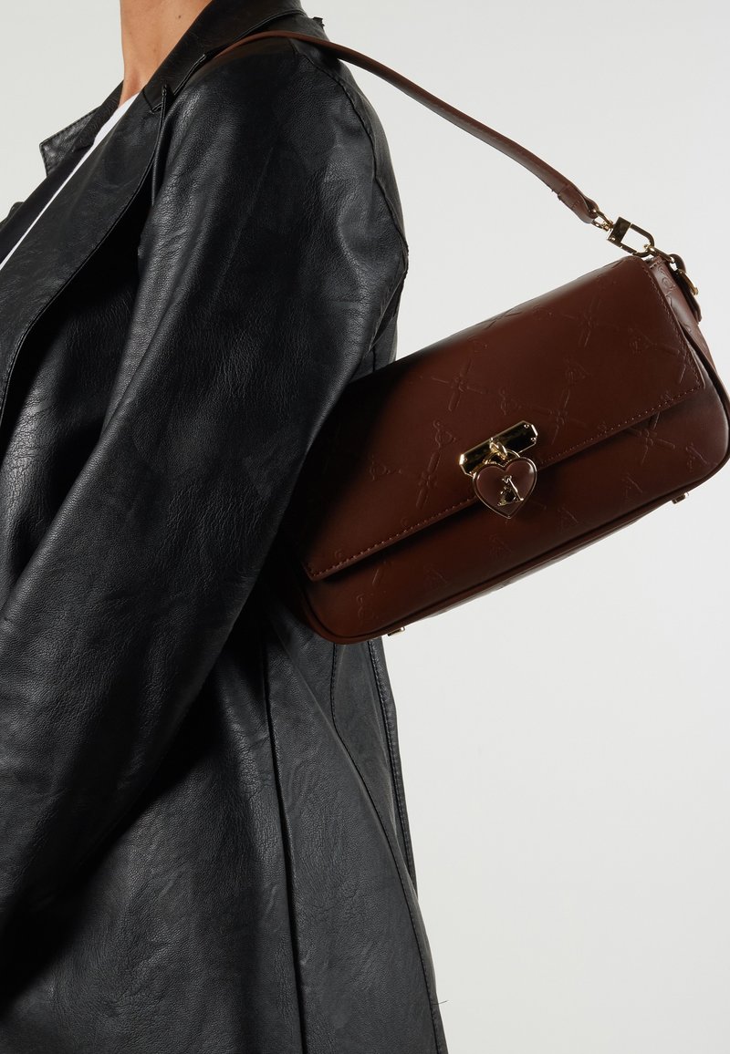 Brown leather handbag with a textured finish, gold hardware, and a heart-shaped clasp detail, worn on the shoulder against a black leather jacket.