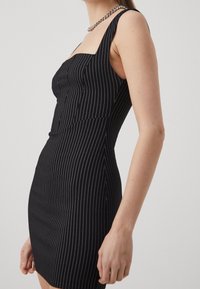 Černé bodycon šaty s bílými vertikálními pruhy, čtvercovým výstřihem a tenkými ramínky. Texturovaná látka s přiléhavým střihem.