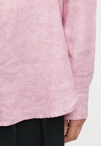 Ροζ πουκάμισο από λινό με απαλή υφή. Διαθέτει καμπυλωτή γραμμή στο τελείωμα και μανσέτα με κουμπί, παρουσιάζοντας ένα διακριτικό σχέδιο ύφανσης.