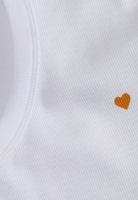 Valge ribadena kangas, millel on peen tekstuur ja väike oranž südame detail. Kaelus on ümmargune ja lihtsa disainiga.