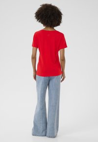 Piros pamut póló rövid ujjakkal, laza fazonban, hátán egy kis dizájn részlettel, világoskék, harangnadrággal párosítva.