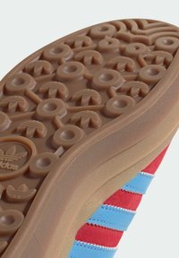 Gummisula med cirkulära och triangulära mönster, med övre del i textil med röda och blå ränder. Sl ät textur med logotypdetalj.