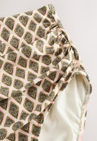 Plavkovina má krémové pozadie s opakujúcim sa vzorom listov v zlatej a námorníckej modrej farbe, so záševkami na boku.