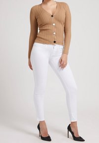 Hnědý žebrovaný pletený cardigan s výstřihem do V, zapínáním na knoflíky a dlouhými rukávy, kombinovaný s bílými skinny džíny a černými lodičkami na vysokém podpatku.