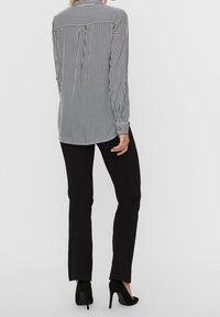Camicia a strisce bianche e nere con maniche lunghe, chiusura con bottoni sul retro e polsini, abbinata a pantaloni neri aderenti e scarpe nere con tacco alto.
