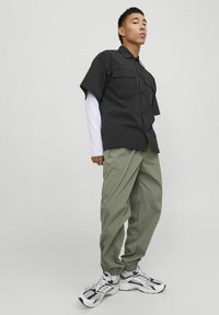 Camisa de botones negra de manga corta con dos bolsillos en el pecho, combinada con pantalones holgados color verde oliva y zapatillas negras y blancas.