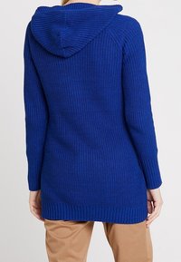 Niebieski dziany sweter z kapturem, z prążkowanymi mankietami i krawędzią, pokazujący teksturowaną tkaninę. Długi krój i swobodny fason.