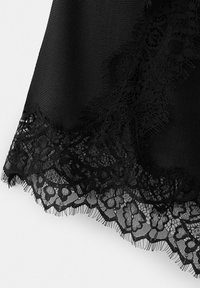 Czarna tkanina z detaliczną koronkową lamówką w kwiatowy wzór na krawędzi, ukazująca kontrast tekstur między gęstym materiałem a delikatnym wzorem koronki.