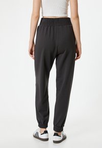 Schwarze Jogginghosen mit einem gerafften Bund, schmal zulaufenden Bündchen und einer glatten Textur, kombiniert mit weißen Sneakers mit schwarzen Akzenten.