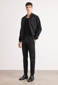 Black bomber jacket with a textured design, paired with a fitted black sweater, slim-fit black trousers, and polished black shoes.