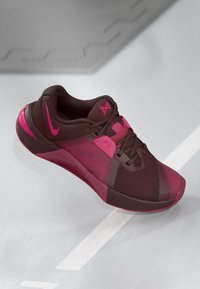 Barna és rózsaszín sportcipő, hálós felsőrésszel, amely texturált mintával, rózsaszín kiegészítőkkel és gumitalppal rendelkezik. A fűzők sötétbarnák.