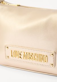 Zlata torbica iz umetnega usnja z teksturirano površino in zlatim znakom s tiskom "LOVE MOSCHINO". Zadrga na vrhu.