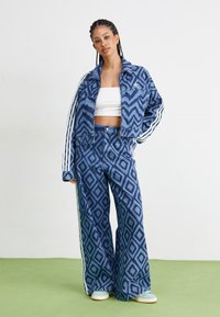 Denimjack en wijde broekset in blauw met een ruitpatroon. De jas heeft een kraag en witte strepen op de mouwen.