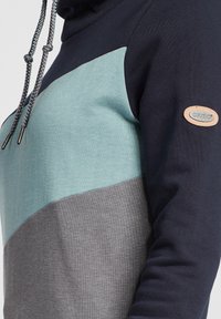 Sweatshirt à capuche avec un design en blocs de couleur navy, sarcelle et gris. Fabriqué en tissu doux avec des cordons de serrage et une badge logo.