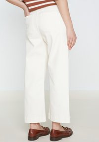 Pantaloni bianchi a gamba larga con una finitura testurizzata, con tasche posteriori e orlo risvoltato. Abbinati a mocassini marroni.