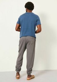 Blaues Baumwoll-T-Shirt mit kurzen Ärmeln, kombiniert mit grauen Sweatpants mit gerippten Bündchen und einer Gesäßtasche, getragen mit beigen Slippern.