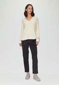 Beige gebreide trui met V-hals en lange mouwen, gecombineerd met zwarte suède broek; grijze platform sneakers maken de outfit compleet.