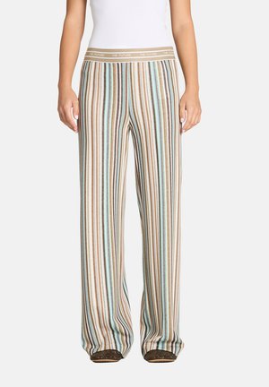 Person trägt eine hochgeschnittene, weit geschnittene Hose mit vertikal gestreiftem Muster in Braun, Blau, Weiß und Beige sowie einem Bund mit der Aufschrift "THE FUTURE".