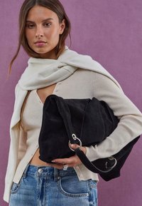 Sac fourre-tout en suède noir avec une texture douce, doté de quincaillerie en argent et d'un design froncé. Accompagné d'un gilet en tricot crème.