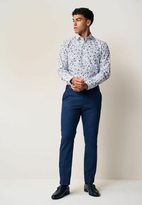 Cămașă albă cu mânecă lungă și model floral albastru, asortată cu pantaloni evazați de culoare bleumarin și pantofi negri, având o croială slim și guler cu nasturi.