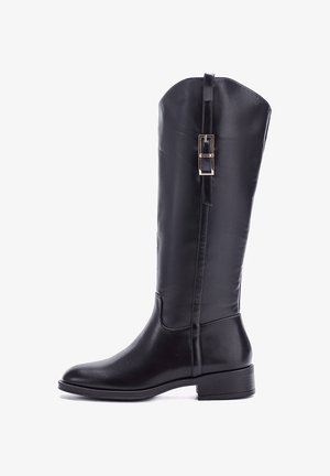 Stivale da equitazione alto in pelle nera con texture liscia, punta arrotondata e tacco basso. Caratterizzato da un accento a fibbia lungo la cucitura laterale.