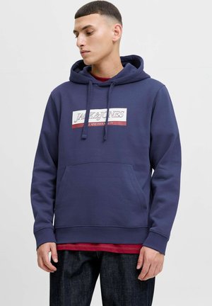 Marineblauwe hoodie met een voorzak, voorzien van een contrasterende logo patch in wit en bordeauxrood. Gemaakt van zachte, gestructureerde stof.