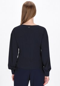 Blusa a maniche lunghe blu navy con scollatura rotonda, maniche arricciate e polsini con bottoni. Tessuto morbido con dettaglio di cucitura centrale sul retro.