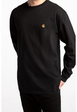 Mężczyzna w czarnej koszulce z długim rękawem z małym żółtym logo Carhartt na lewej piersi, ręce z tyłu, na jednolitym białym tle.
