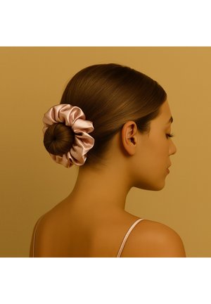 Satin scrunchie in soft pink holds a bun of brown hair, set against a warm beige background, emphasizing smooth textures and subtle shine.