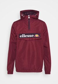 Burgundy water-resistant jacket with a half-zip front, elastic cuffs, and a large black logo patch across the chest, featuring a colorful design.