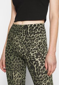 Leggings de estampa de leopardo verde feitos de material elástico, com uma cintura alta e um top cropped preto com texturização, expondo a barriga.