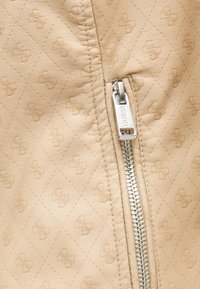 Μπεζ καπιτονέ δερματίνη ύφασμα με διακριτικά ανάγλυφα λογότυπα GUESS και ασημένια τσέπη φερμουάρ με χαραγμένη την επιγραφή "GUESS".
