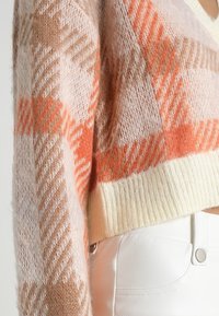 Maglione lavorato a maglia con un motivo a scacchi rosa e arancione, con orlo a coste color crema e una texture morbida e pelosa.