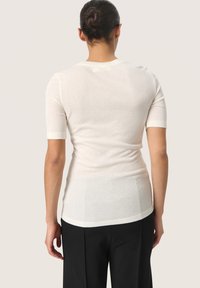 Witte, aansluitende top met korte mouwen en een ronde halslijn, zachte textuur en een gladde afwerking, gecombineerd met losse zwarte broek.