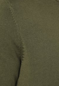 Olivgrön stickad textil som visar en närbild av texturen, med synliga stygn och jämn väv.