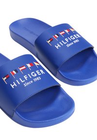 Niebieskie klapki z teksturowaną gumową podeszwą i szerokim paskiem. Posiadają haftowane flagi oraz napis "HILFIGER Since 1985" na pasku.