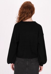 Schwarzer gestrickter Pullover mit lässiger Passform, Fledermausärmel und strukturiertem Muster. Darunter befindet sich ein dunkelgraßer Jeansrock mit minimalen Details.