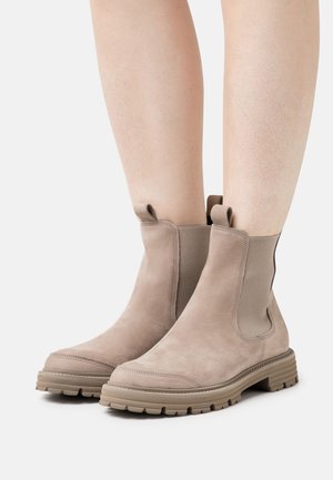 Stivaletti alla caviglia in suede beige con pannelli elastici laterali, suola in gomma testurizzata e linguette per una facile calzata. Progettati per il comfort e la stabilità.