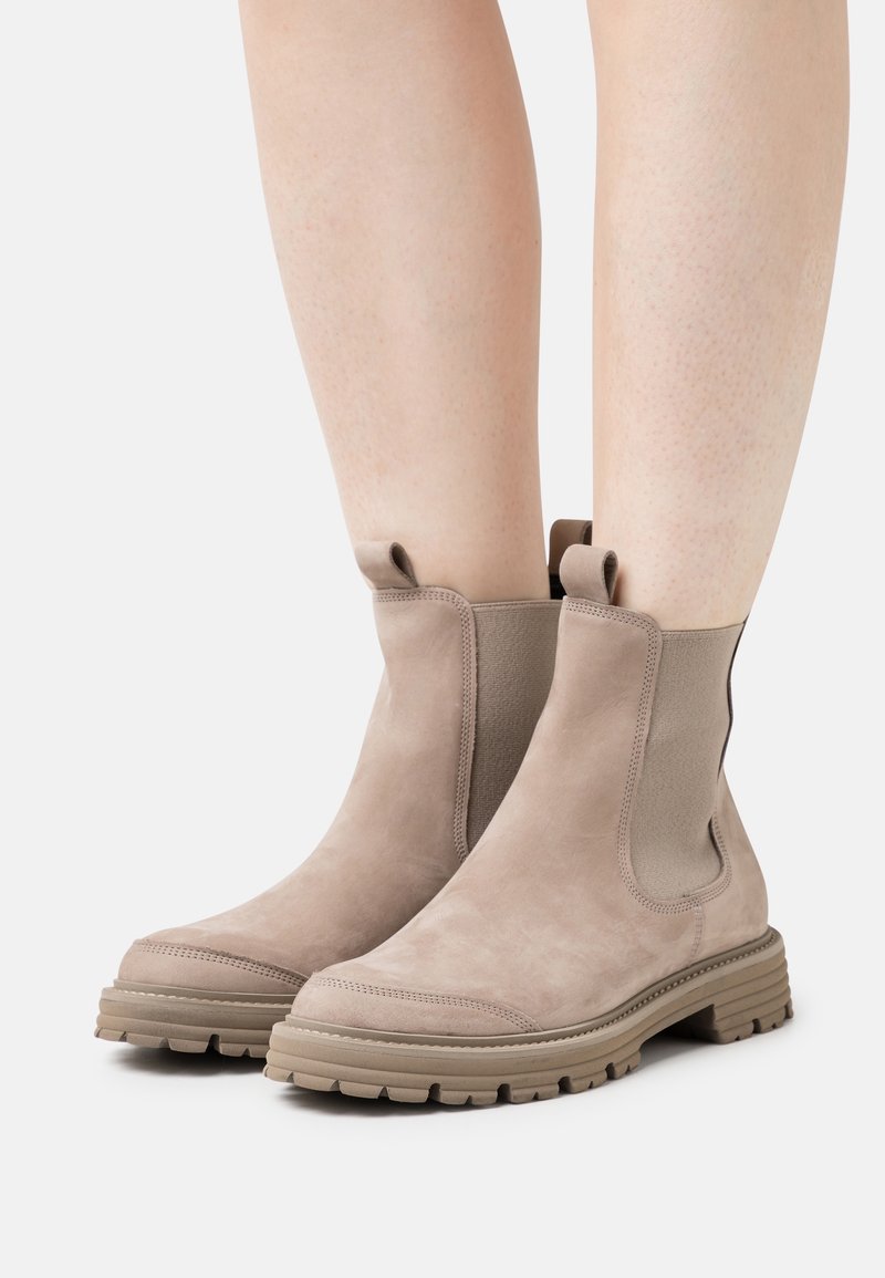 Stivaletti alla caviglia in suede beige con pannelli elastici laterali, suola in gomma testurizzata e linguette per una facile calzata. Progettati per il comfort e la stabilità.