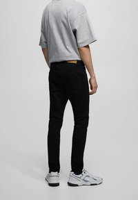 Pantalones vaqueros negros de corte ajustado, confeccionados en denim, combinados con una camiseta gris de manga corta y zapatillas blancas. Detalles notables en los bolsillos traseros.