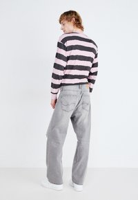 Camisa de rayas de manga larga en negro y rosa, combinada con jeans gris deslavado de corte holgado que cuentan con bolsillos traseros y una etiqueta de cuero.