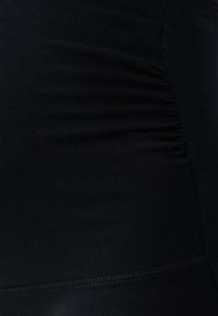 Nahaufnahme eines schwarzen Stoffs mit gesammelten elastischen Nähten auf einer Seite, die eine dezente Textur und Form erzeugen.