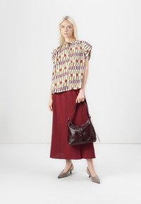 Multicolored patterned blouse with short sleeves, paired with a long burgundy skirt. Carrying a dark red leather shoulder bag. taupe heels.