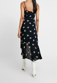 Vestido negro con flores y tirantes finos, con un dobladillo con volantes y una tela ligera y fluida. Pequeños patrones florales en blanco y amarillo a lo largo.