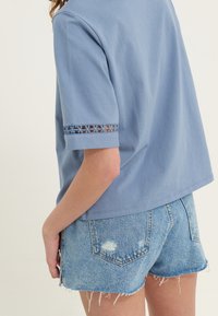 Ljusblå bomullstopp med korta ärmar och spetsdetaljer, kombinerad med slitna denimshorts. Texturerad tyg med avslappnad passform.