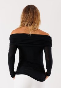 Top nero senza spalle con maniche lunghe, scollatura arricciata e design aderente. Il materiale appare liscio e leggermente texturizzato.