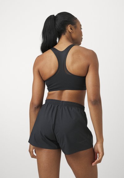Sujetador deportivo negro con diseño de espalda de nadador y detalles de malla, combinado con pantalones cortos negros que cuentan con una cinturilla elástica. Textura suave en general.