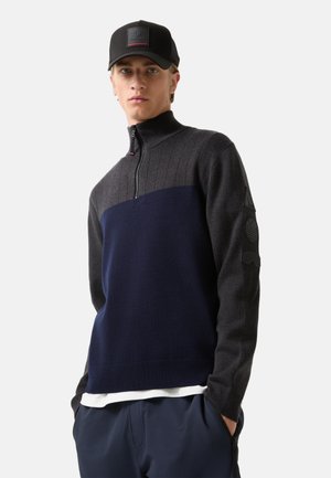 Dunkelgrauer und marineblauer Zip-Kragen-Pullover mit gerippter Textur und besticktem Logo am Ärmel, kombiniert mit einer schwarzen Mütze mit Logopatch.