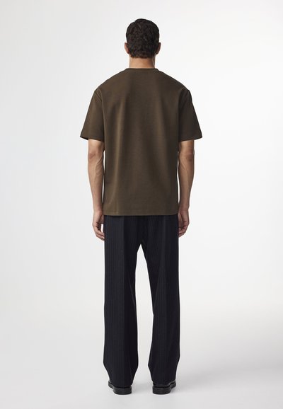 Oliven grøn kortærmet t-shirt med en afslappet pasform, parret med sorte pinstribede vidde bukser, set bagfra.